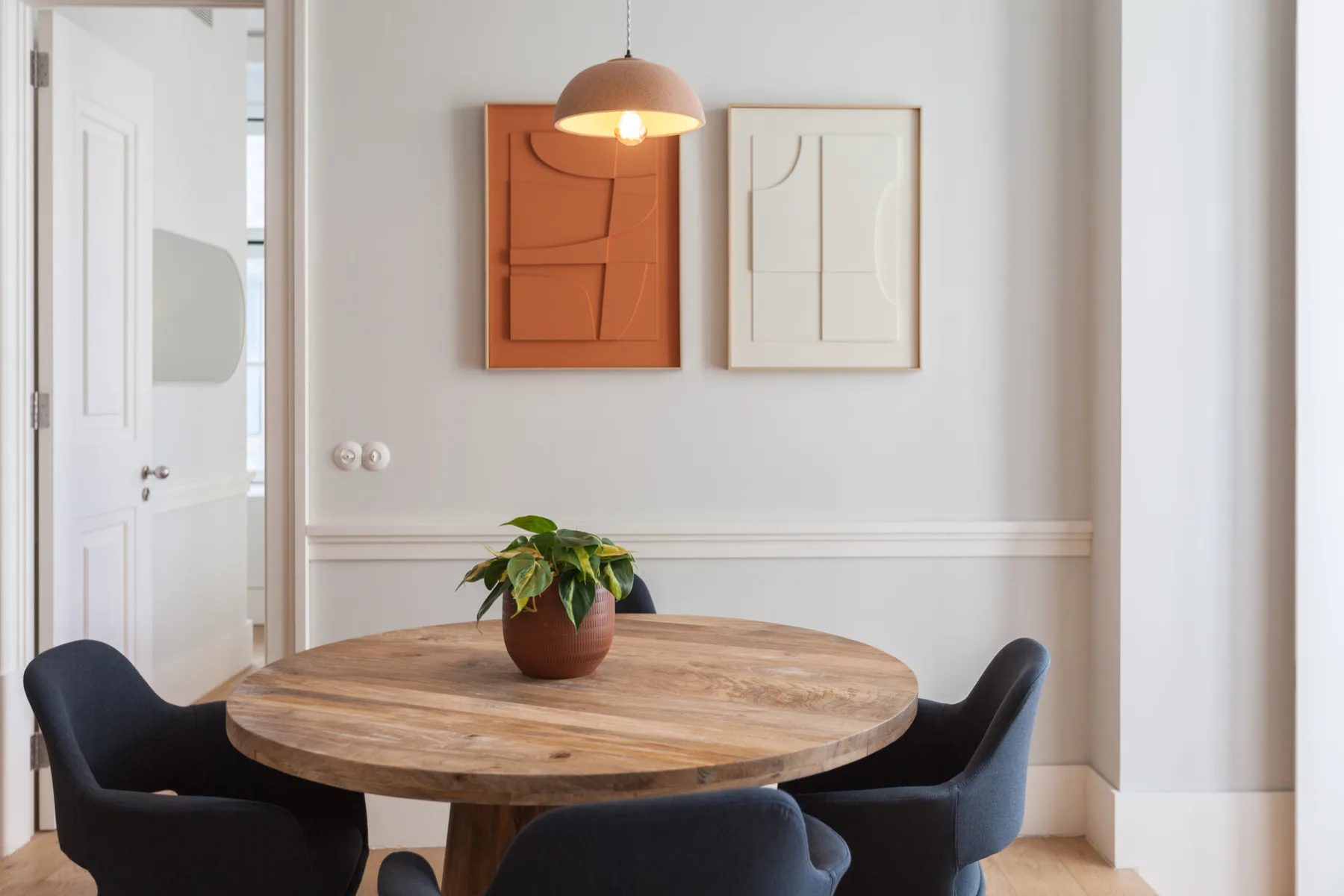 Comedor con mesa redonda de madera, asientos oscuros y cuadros en la pared.