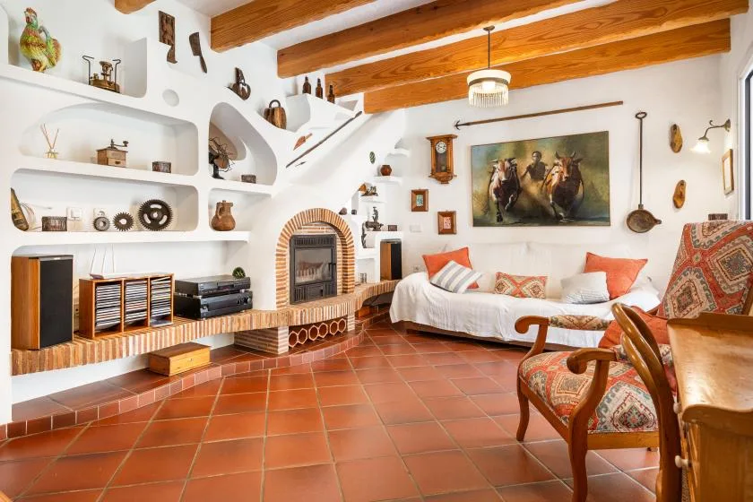 A living room with built-in shelves, a tiled floor, and wooden ceiling beams.