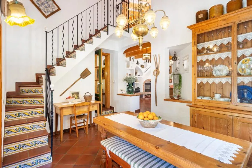 A dining area with a long wooden table and a staircase in the background.