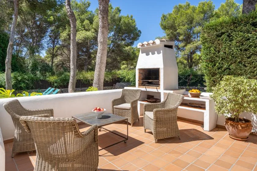 A tiled outdoor patio has wicker seating, a table, and a built-in barbecue.