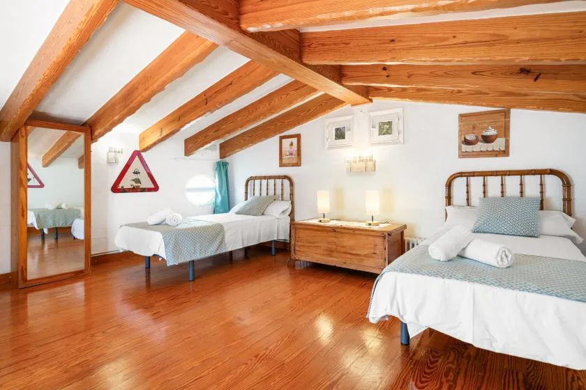 A bright bedroom with two beds, wooden ceiling beams, and polished wood flooring.
