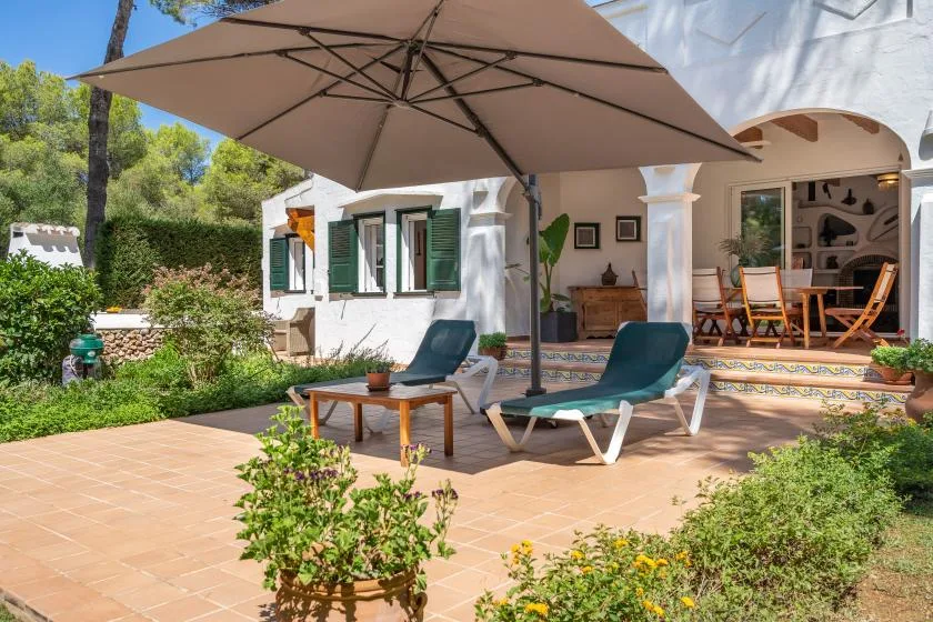A sunny patio with reclining seating, an umbrella, and an open dining area.