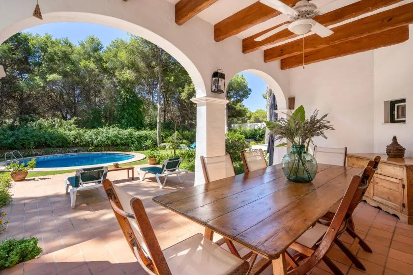A covered outdoor dining area opens onto a garden and swimming pool.