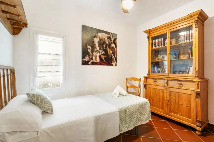 A bedroom with a neatly made bed, a window, and a wooden cabinet.
