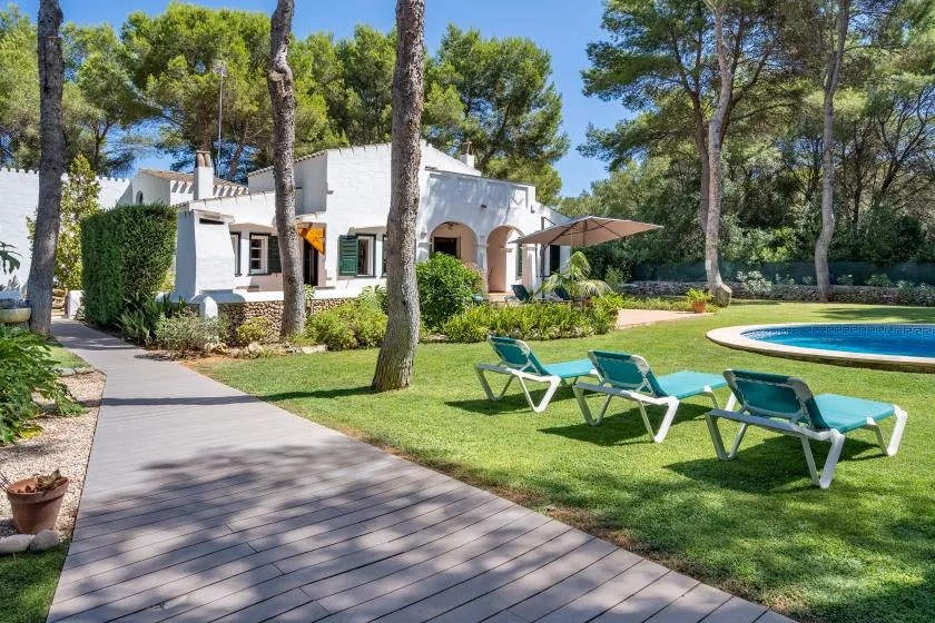 A white house and swimming pool sit beside a garden path and lawn.
