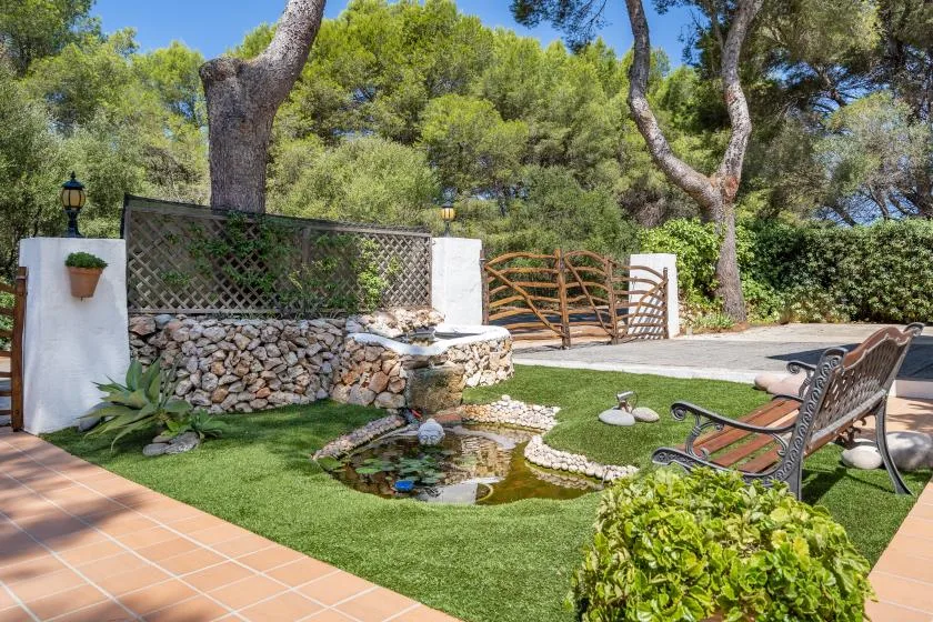 A landscaped garden patio with a small pond, seating, and surrounding trees.