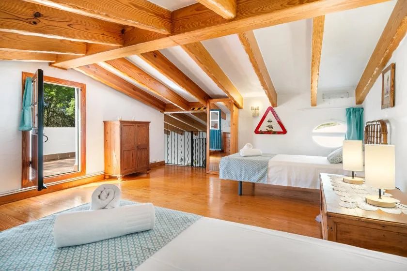 A bright bedroom with exposed wooden beams, a bed, and a large window.
