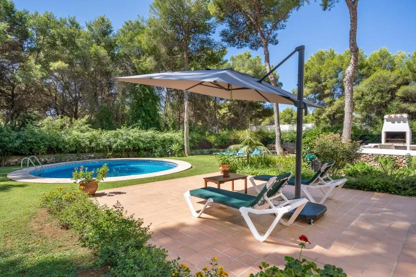 An outdoor pool and patio with lounge seating beneath a large shade umbrella.