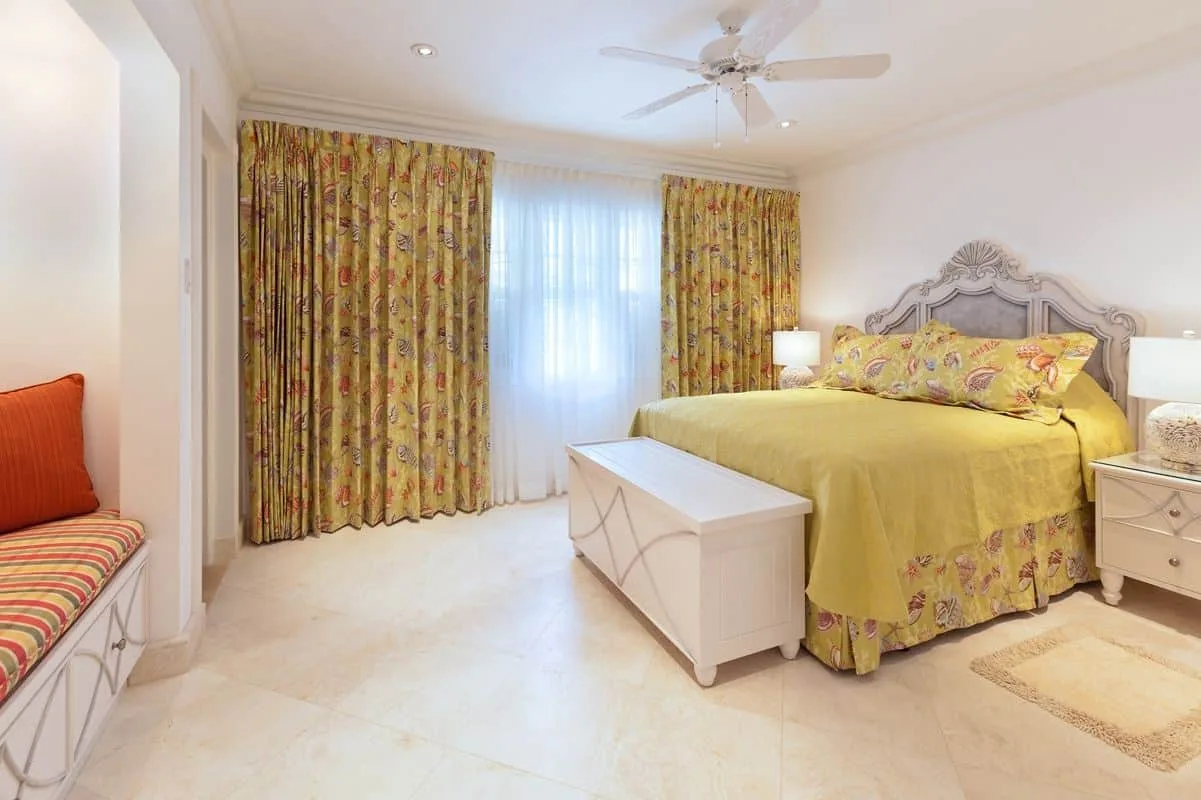 Un dormitorio con colcha y cortinas florales, y un banco blanco de almacenaje.