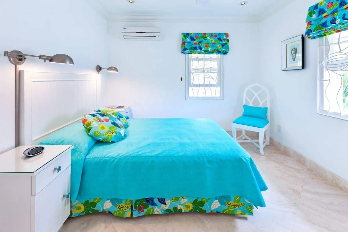 Un dormitorio con una colcha turquesa y cenefas coloridas en las ventanas.