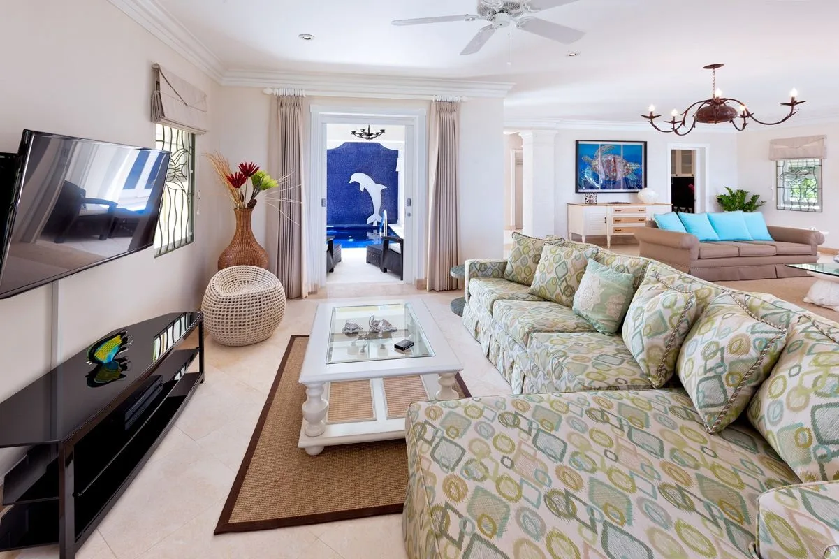 Una sala luminosa con asientos estampados, una mesa de centro de vidrio y un televisor en la pared.
