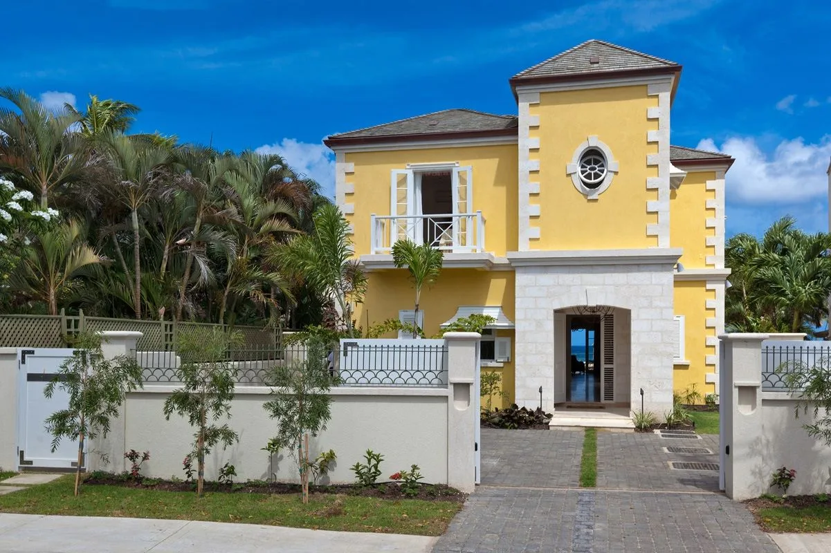 A yellow house with a gated entrance and a paved path leading to the front door.