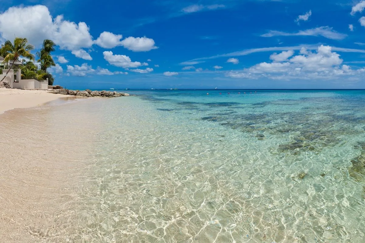 A sandy beach meets clear, shallow turquoise water beneath a blue sky.