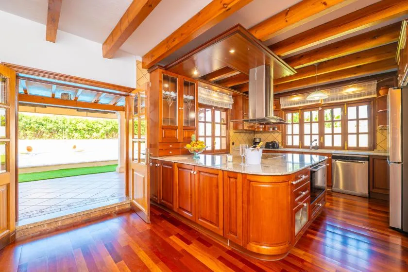 Una cocina con gabinetes de madera, una isla central y ventanas en la pared del fondo.