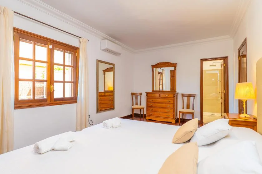 Un dormitorio luminoso con una cama grande, una cómoda de madera y una ventana.