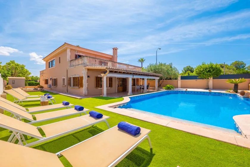 Una villa y una piscina están junto a un césped con tumbonas.