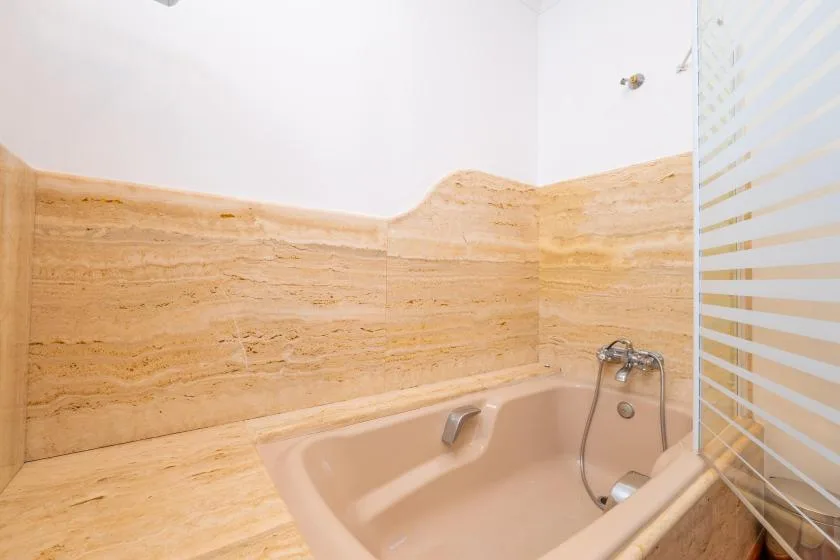 Un baño con bañera, azulejos beige y una mampara de vidrio a rayas.