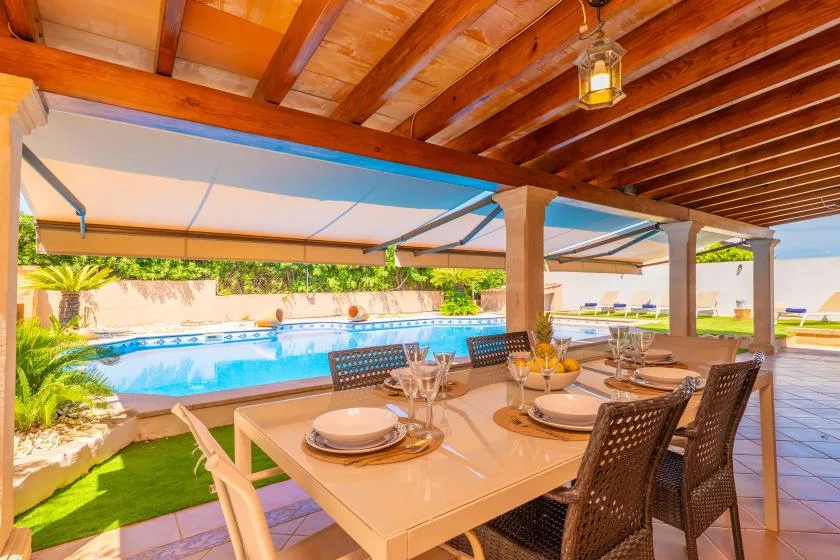 Una zona de comedor exterior cubierta da a una piscina.
