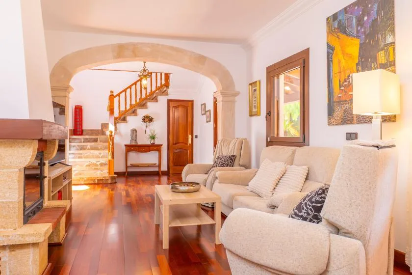 Una sala luminosa con asientos, una mesa de centro y una escalera al fondo.