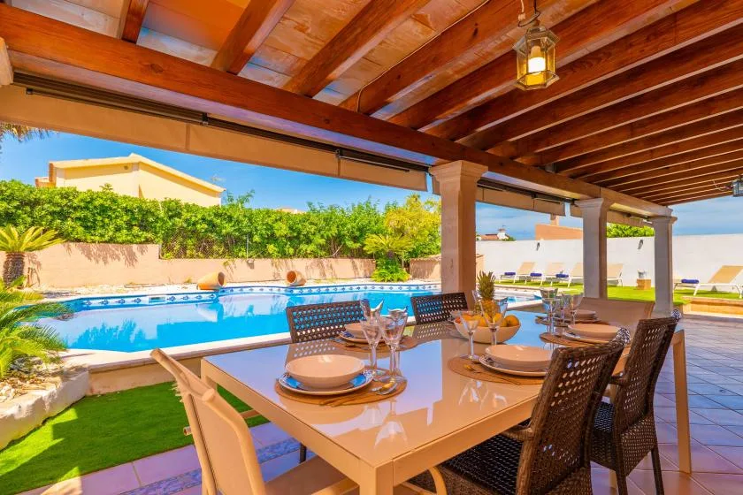 Una zona de comedor exterior cubierta da a una piscina y un seto verde.