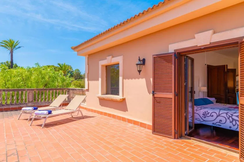 Una terraza soleada con asientos de descanso da a la vegetación junto a una puerta abierta al dormitorio.