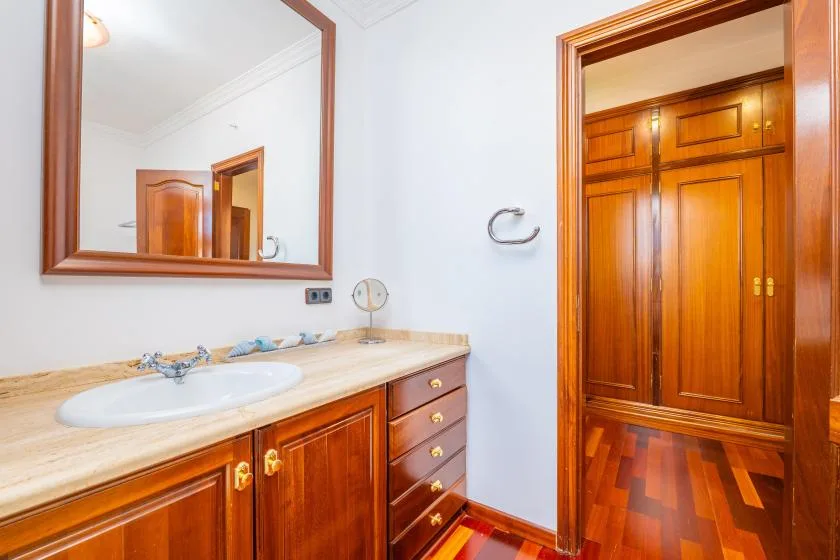 Un lavabo de baño con mueble de madera junto a una puerta abierta.