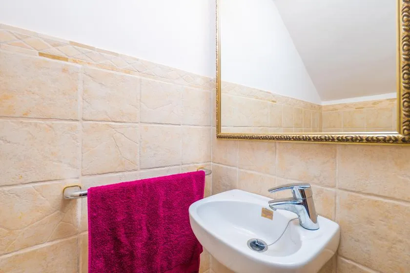 Un lavabo de baño está debajo de un espejo de pared, con una toalla de color vivo cerca.