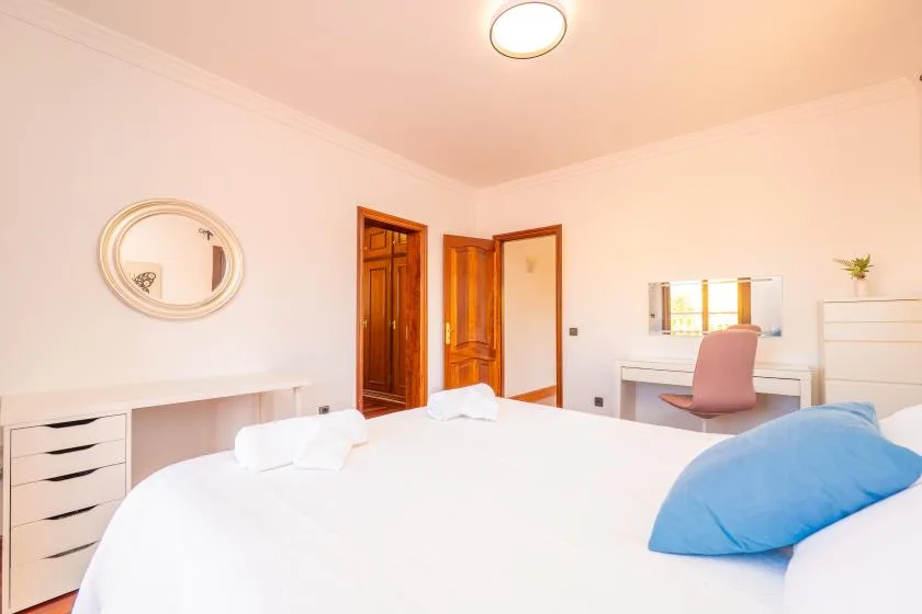 Un dormitorio luminoso con una cama, un escritorio y una silla rosa.