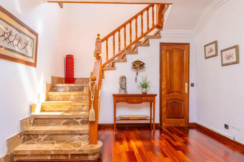 Una escalera interior con barandilla de madera, una consola y una puerta cerrada.