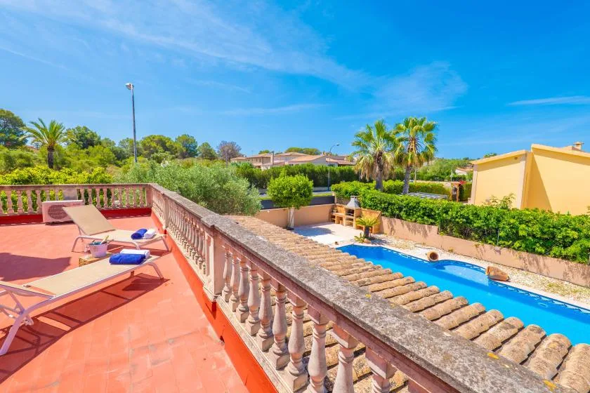 Una terraza soleada tiene vistas a una piscina y a la vegetación circundante.