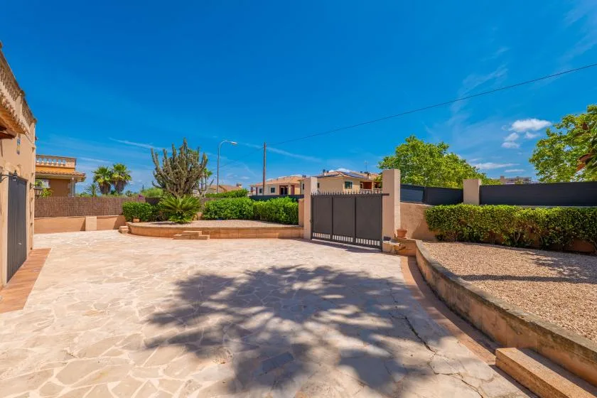 Un patio exterior pavimentado con una puerta oscura y parterres con plantas.