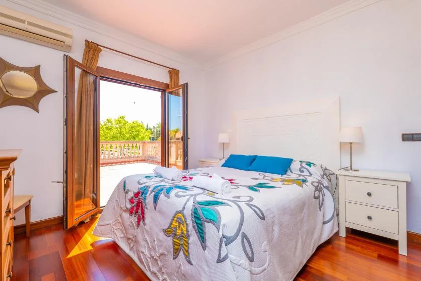 Un dormitorio con una cama vestida con ropa de cama estampada y la puerta del balcón abierta.