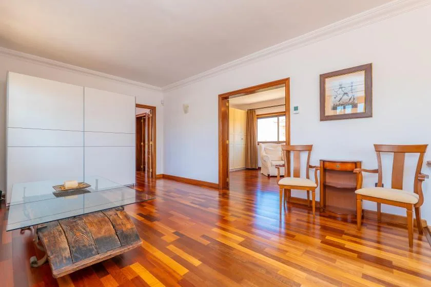 Un comedor luminoso con una mesa de vidrio, asientos de madera y puertas abiertas.