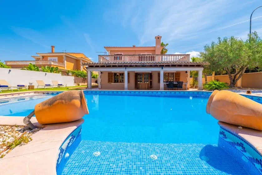 Una piscina frente a una casa, con asientos junto al lado opuesto.