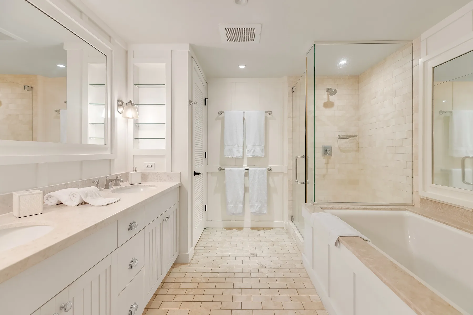 A bright bathroom with a long vanity, bathtub, and glass shower.