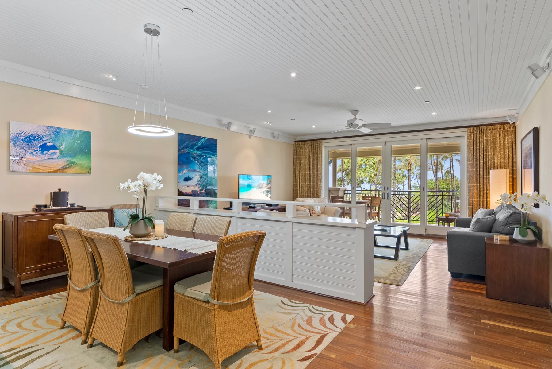 An open-plan living and dining room has seating beside windows overlooking greenery.
