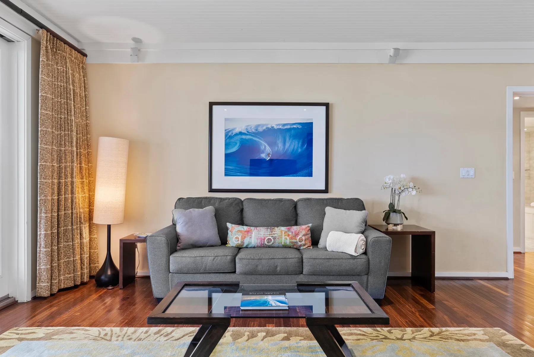A living room with gray seating, a glass coffee table, and framed artwork.