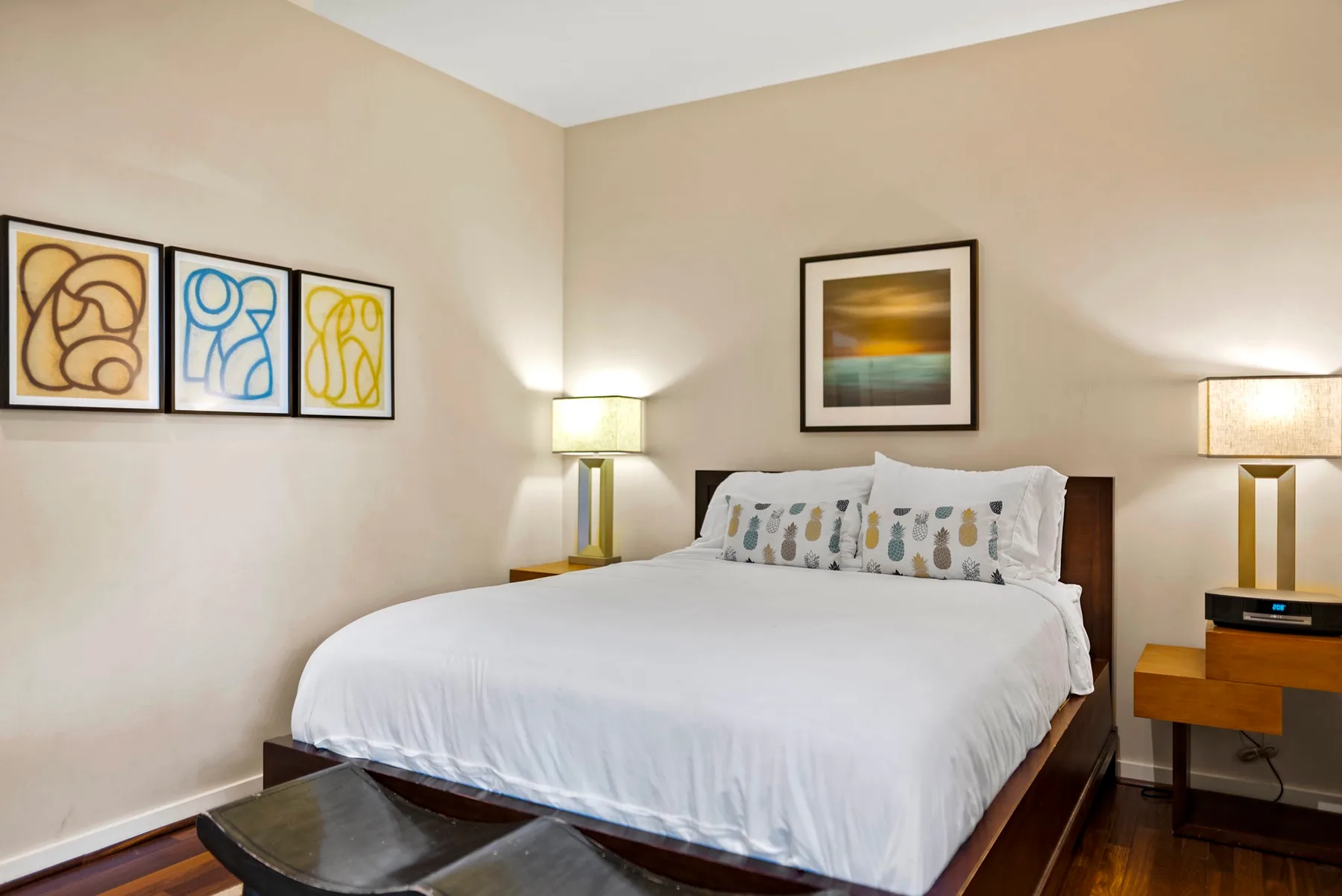 A bedroom with a neatly made bed, bedside lamps, and framed artwork.