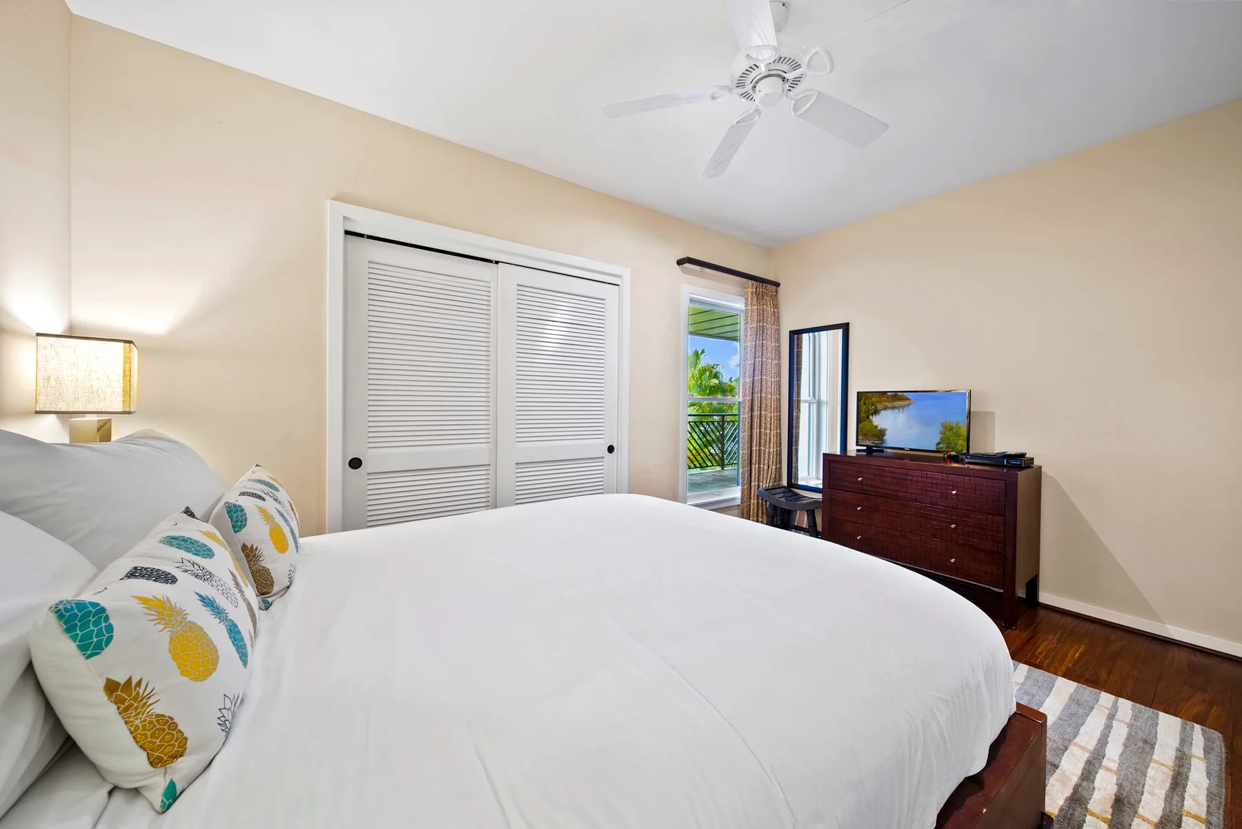 A bedroom with a large bed, sliding closet doors, and a dresser with a television.