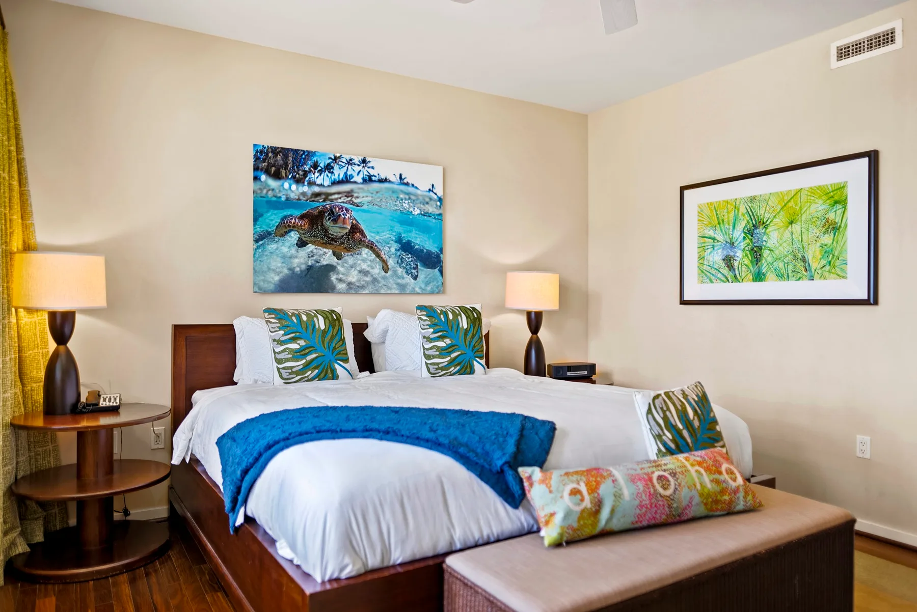 A bedroom with a neatly made bed, colorful pillows, and framed wall art.
