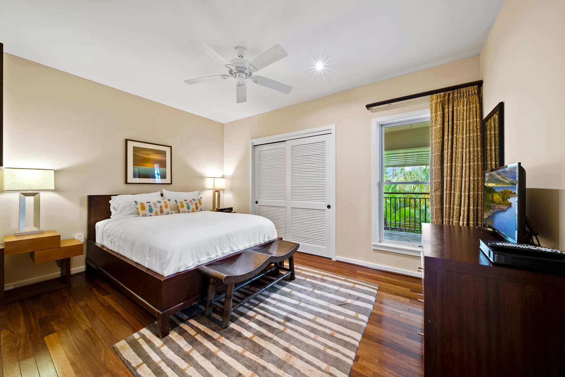 A bedroom with a bed, a ceiling fan, and a window overlooking greenery.