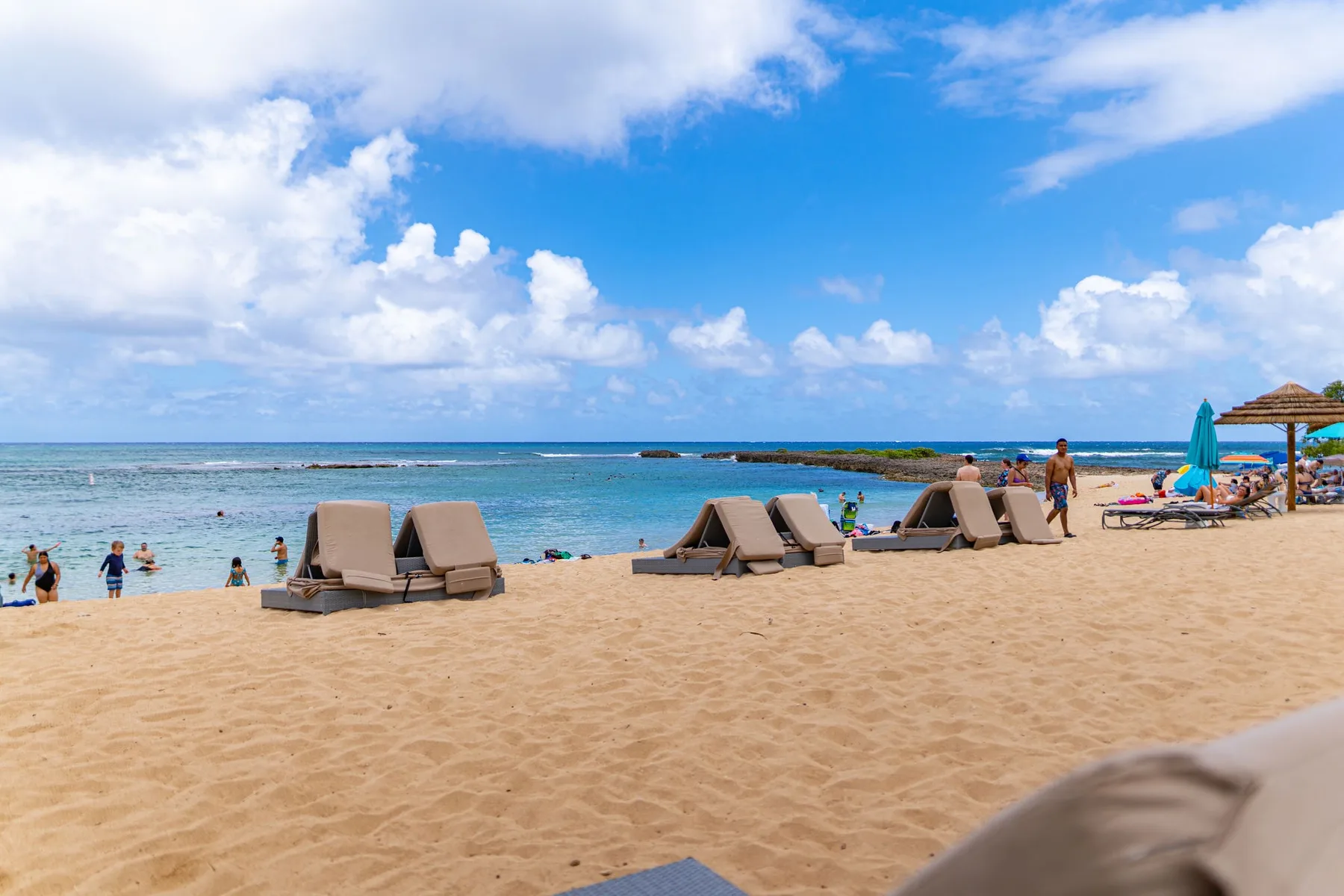 A sandy beach with lounge seating beside the ocean under a partly cloudy sky.