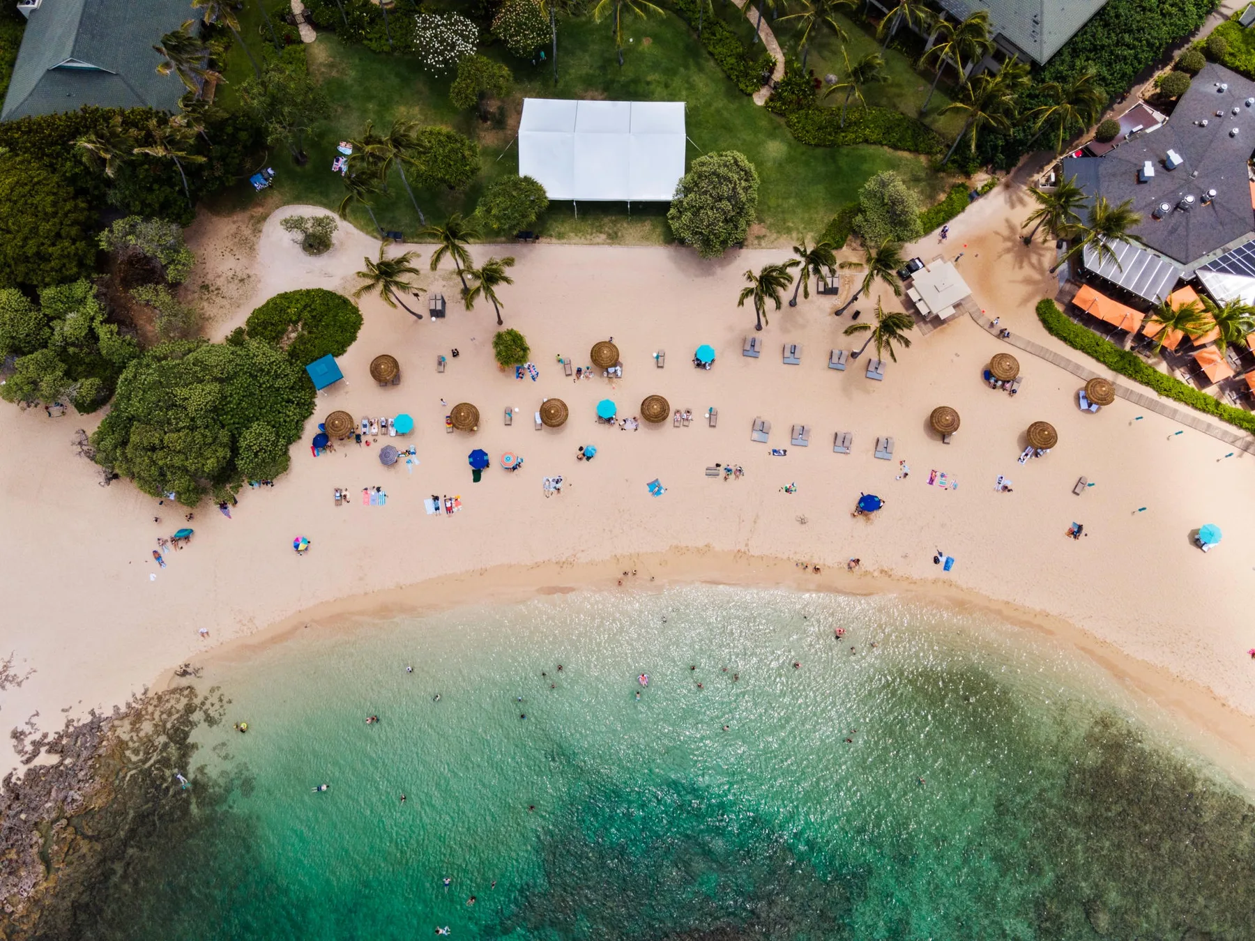 Aerial view of a sandy beach with people, umbrellas, and clear water.
