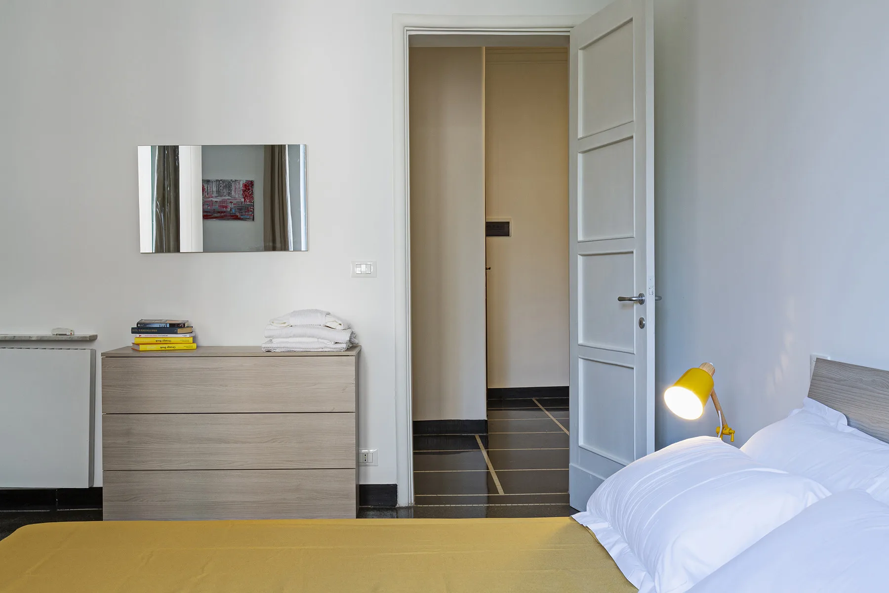 A bedroom with a bed, bedside lamp, and dresser beside an open doorway.