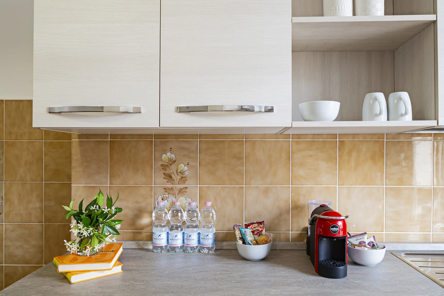 A kitchen counter with white cabinets, cups, and a small coffee machine.