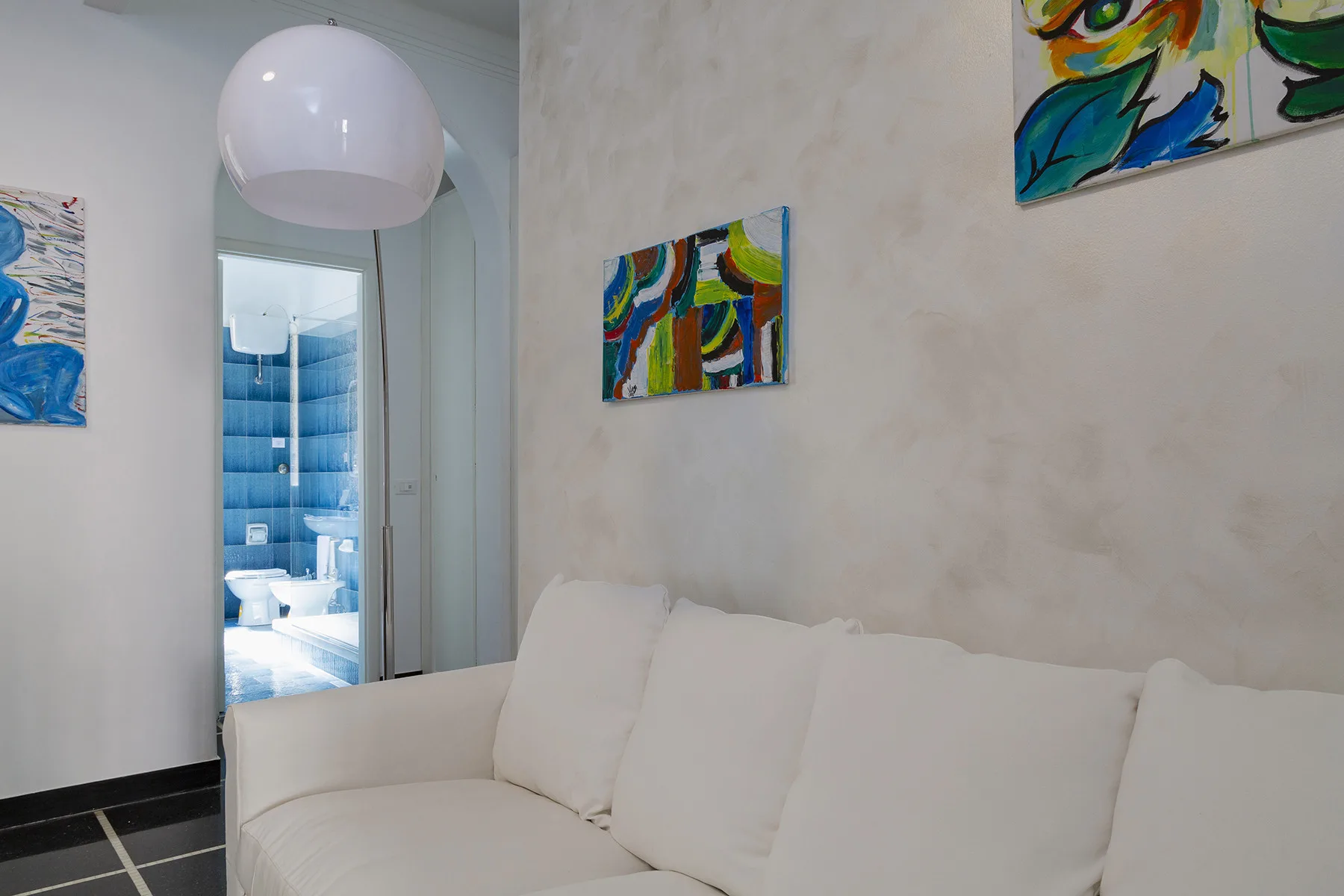 A bright seating area with a white sofa and colorful abstract paintings.