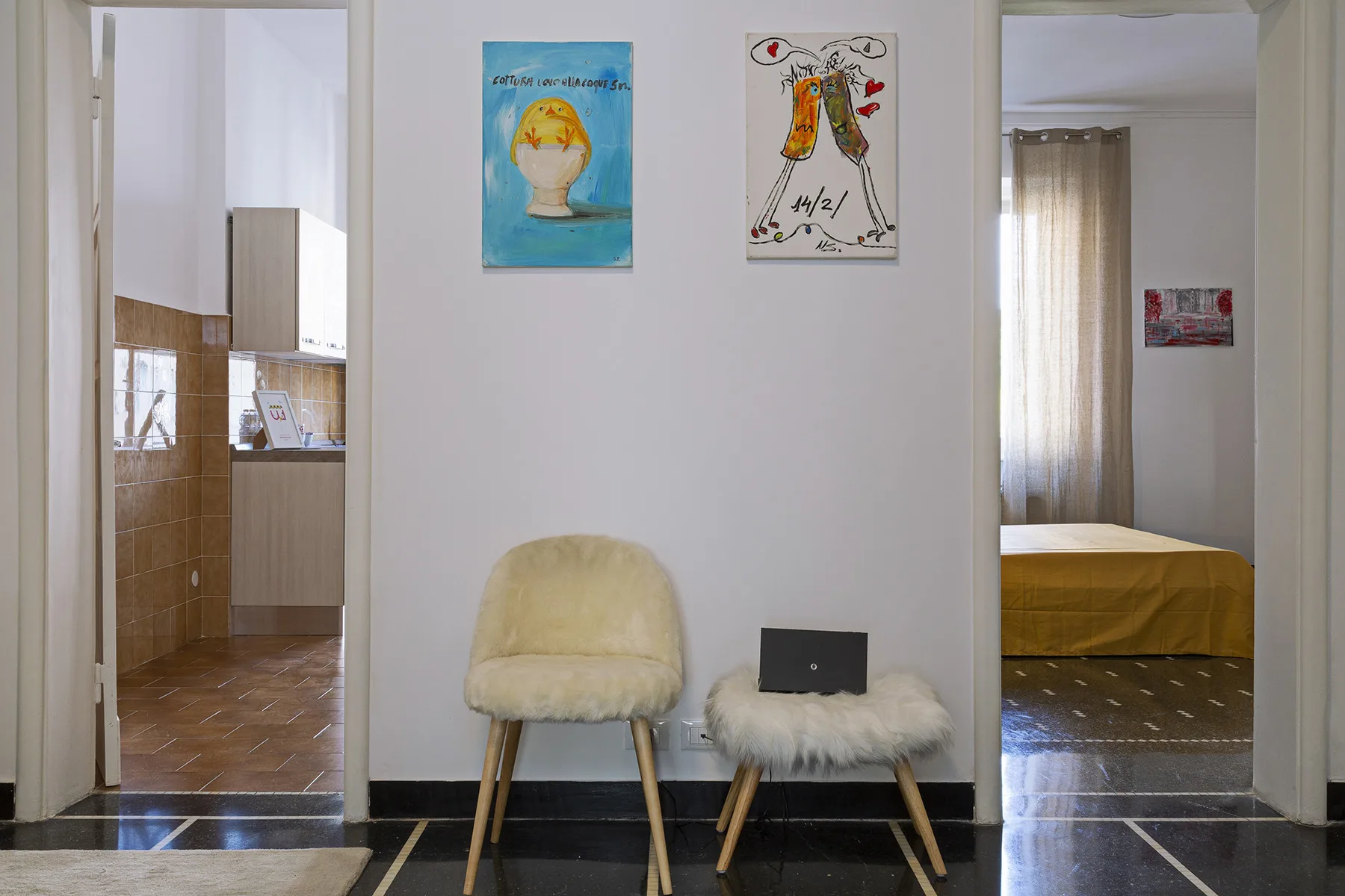 A hallway with two small seats beneath colorful wall art, between open doorways.