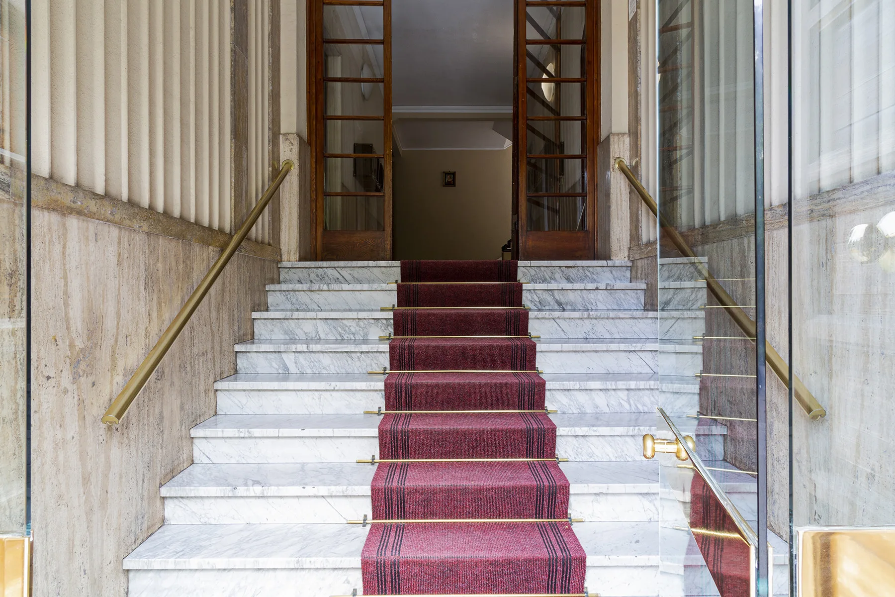 A marble staircase with a red runner leads to an open doorway.