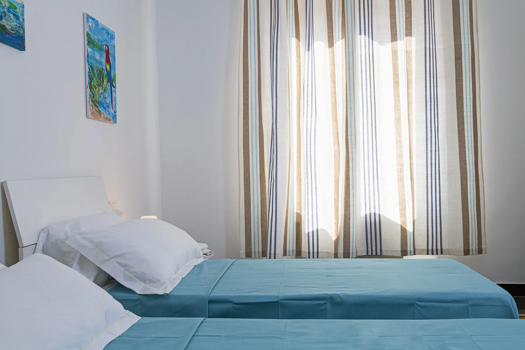 A bedroom with beds covered in blue bedding beside striped curtains.