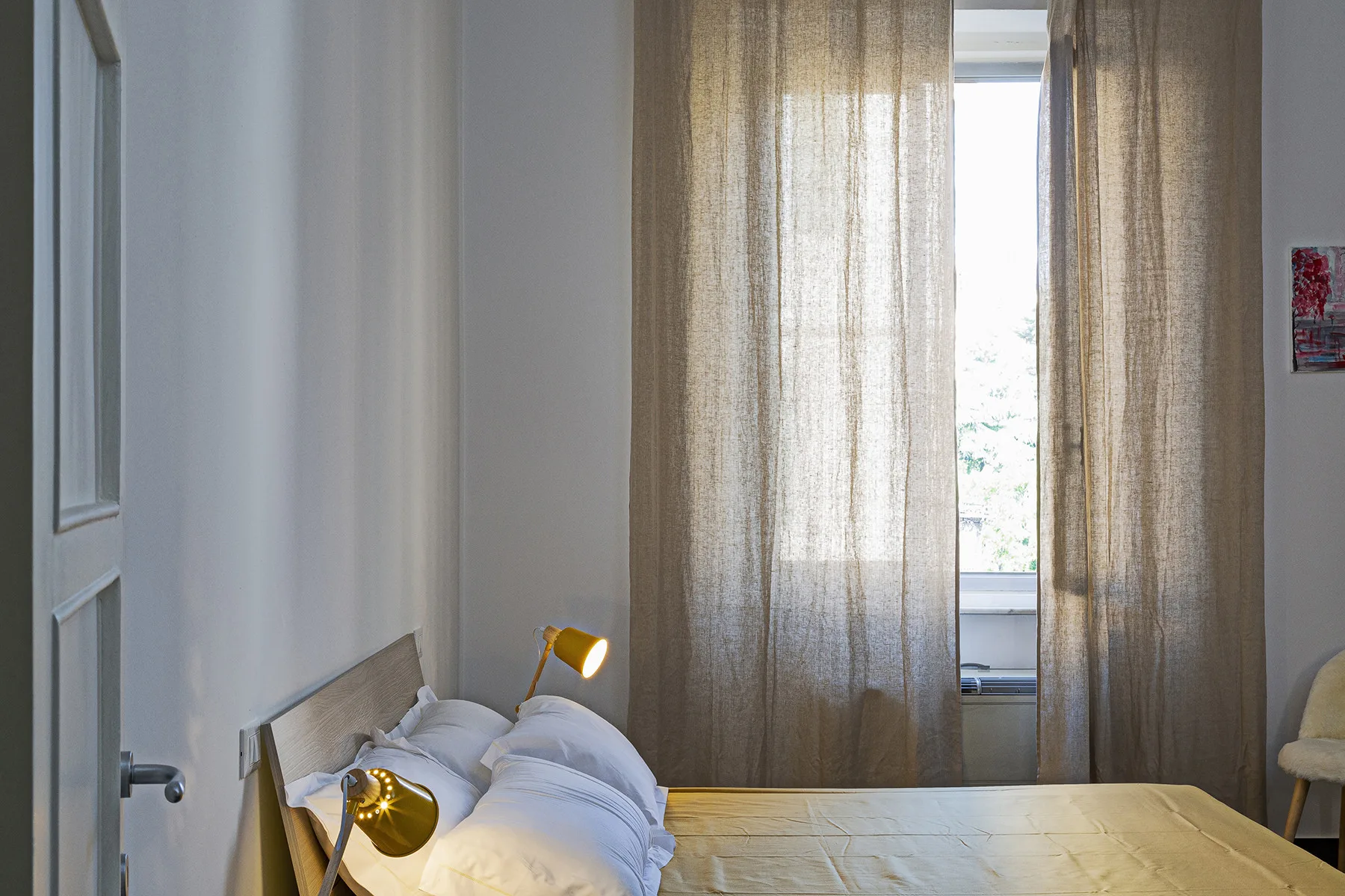 A bedroom with a bed beside a tall window covered by curtains.